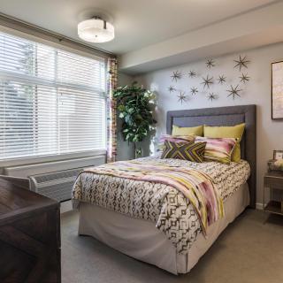 A modern bedroom with a single bed, decorative pillows, and star-shaped wall art, illuminated by natural light through a large window.