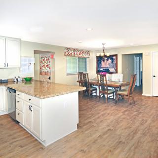 A spacious kitchen with a dining area featuring wood flooring, a central kitchen island, and white cabinets.