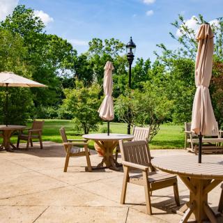 A sunny outdoor patio area with tables, chairs, and umbrellas overlooking a lush garden.
