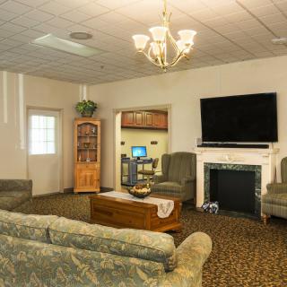 A cozy living room featuring a chandelier, large flat-screen television, fireplace, and comfortable seating arrangements.