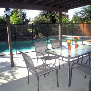 A backyard patio with outdoor furniture overlooking a swimming pool with a safety fence.