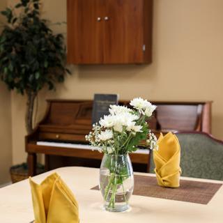 A cozy dining area featuring a vase of flowers, neatly arranged napkins, and a piano in the background.