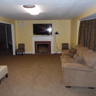 A spacious living room with a sofa, carpet, wall-mounted television, and a decorative fireplace.