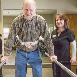 A patient engages in a physical therapy session using walking bars, supported by a healthcare professional.
