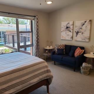 A cozy bedroom with a bed and seating area near a large window, featuring abstract artwork on the wall.