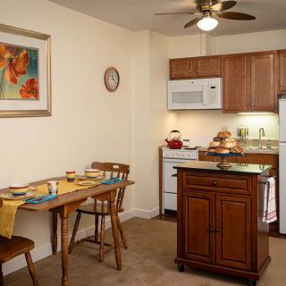 A cozy kitchen and dining area with a small table set for two, featuring wooden cabinetry, a ceiling fan, and a compact kitchen island.