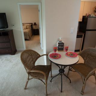 A cozy apartment interior featuring a small dining area with a round table and chairs, adjacent to a kitchen and bedroom.