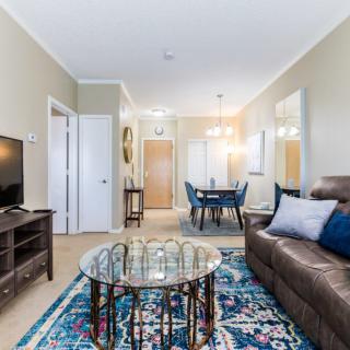 A cozy living room with a brown sofa, glass coffee table, and a colorful rug, leading to a small dining area.