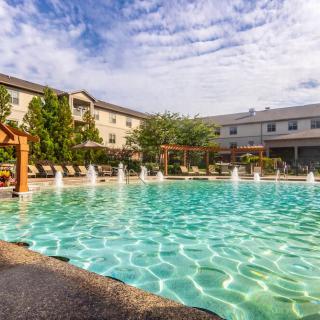 A scenic view of a hotel resort with a large outdoor swimming pool and fountains, set against a clear sky.
