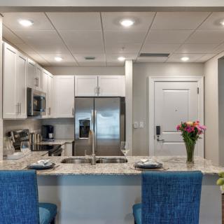 A modern kitchen interior with a marble countertop, blue bar stools, and stainless steel appliances.