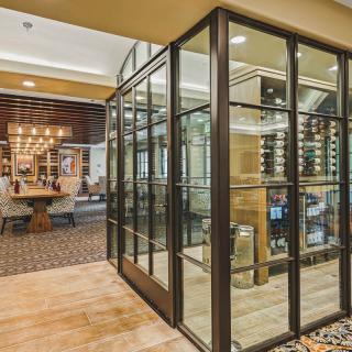 A modern restaurant interior featuring a glass-enclosed wine cellar and seating area.