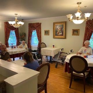A cozy dining room with seniors seated at tables, adorned with elegant chandeliers and red curtains.