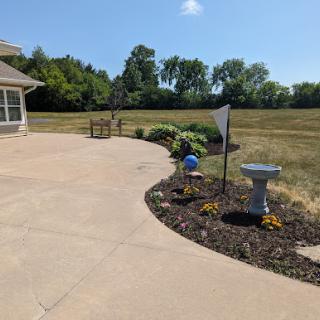 A serene outdoor patio area featuring a well-kept garden, birdbath, and open field in the background.