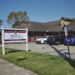 A clinic building with a sign in front and cars parked in the lot.