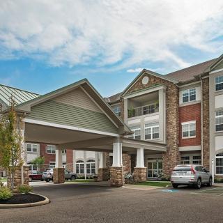 A residential building with a covered entrance and parked cars in the driveway under a partly cloudy sky.