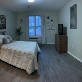 A cozy bedroom with a neatly made bed, wooden flooring, and a television on a dresser.