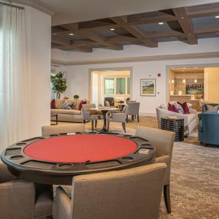 A modern game room featuring a red-padded poker table surrounded by comfortable chairs.