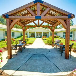 A scenic outdoor area featuring a wooden gazebo, surrounded by benches and landscaped gardens.