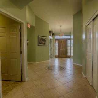 A spacious hallway with tiled flooring leading to a wooden front door, illuminated by overhead lighting.