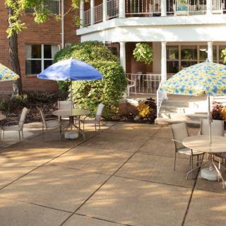 Outdoor patio area with tables, chairs, and umbrellas surrounded by greenery.