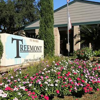 Entrance to a building with a garden of colorful flowers and a prominent sign.