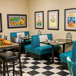 A retro-style diner with teal booths and checkered flooring, featuring vintage posters on the walls.