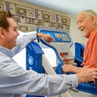 An elderly man smiling during a rehabilitation session with a therapist.