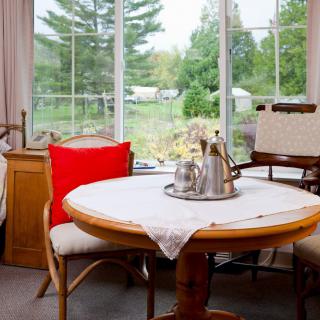 A cozy dining area with a round table and chairs, featuring a tea set, situated near a large window with a scenic outdoor view.