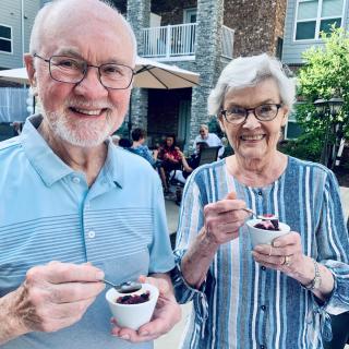 An elderly couple enjoying dessert outdoors on a sunny day.