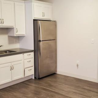 A modern kitchen featuring white cabinets, stainless steel refrigerator, and wood flooring.