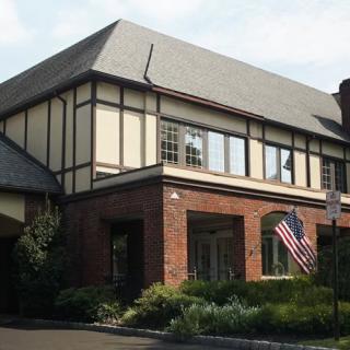 A traditional Tudor-style building with an American flag beside a landscaped garden.