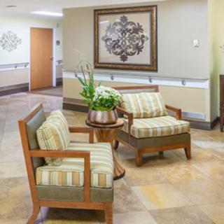 A cozy waiting area featuring two cushioned chairs and a small table with a potted plant, set against a warmly decorated wall.