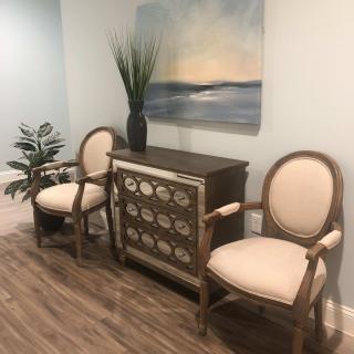 A stylish interior with two elegant chairs, a decorative console table, a plant, and a serene landscape painting.