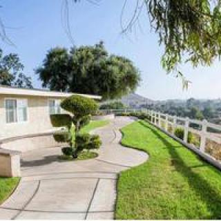 A scenic view of a house with a landscaped garden, featuring a curving pathway and white fence.