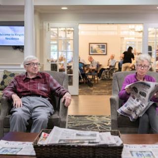 Two seniors relax in a cozy lounge area, reading newspapers and enjoying their time together.