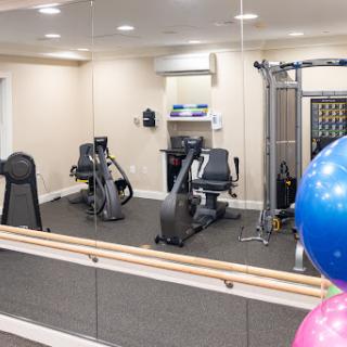 A well-equipped indoor gym featuring exercise bikes and a multi-station weight machine, complete with mirrors and colorful workout balls.