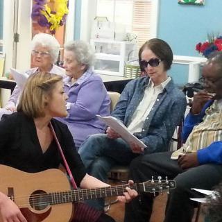 A group of people gathered for a musical session, with one playing the guitar.
