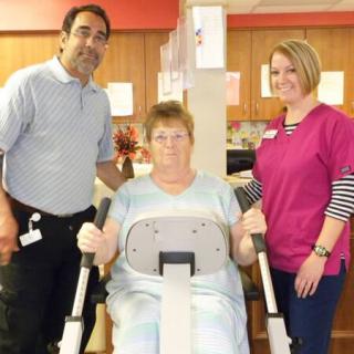 A patient exercising on a rehabilitation machine with the assistance of two healthcare professionals.