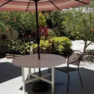 A sunny patio with a table and chairs under an umbrella surrounded by a garden.