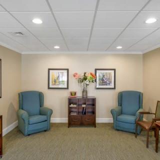 A cozy waiting room with blue armchairs, artwork on the walls, and a small table adorned with flowers.