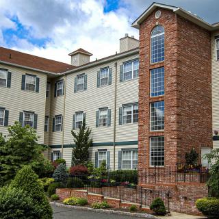 A residential building with brick and siding exterior, surrounded by gardens.