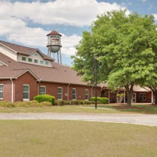 A brick building with a water tower in the background, surrounded by trees and a cloudy sky.