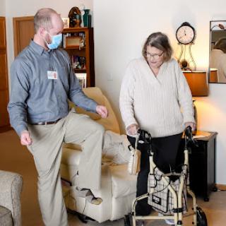 A healthcare professional assists a woman using a walker in a living space, highlighting the importance of mobility support for elderly individuals.