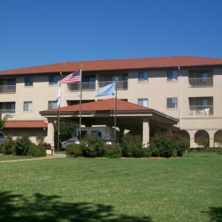 A hotel building with a red roof, flags at the entrance, and a well-maintained lawn under a clear blue sky.