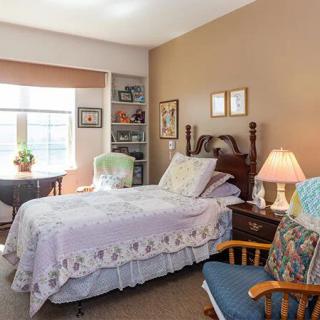 A cozy bedroom with a single bed, a bedside table with a lamp, and a comfortable chair by the window.