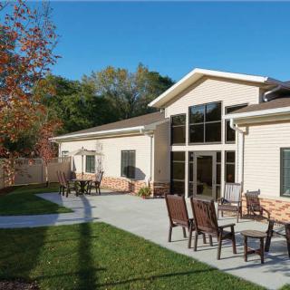 A modern building with a patio area featuring outdoor seating, surrounded by grass and autumn trees.