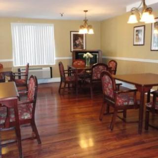 A cozy dining room with wooden tables and chairs, featuring elegant lighting and a hardwood floor.