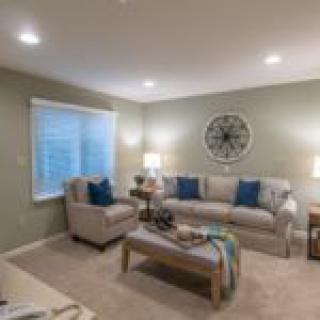 A cozy living room featuring a sofa, armchair, and a coffee table, decorated with lamps and a wall clock.