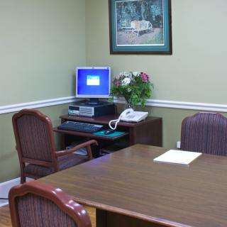 A small office meeting room with a desk, computer, chairs, and a telephone.