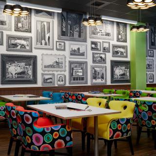 A modern restaurant interior featuring colorful chairs and a wall adorned with framed artwork.